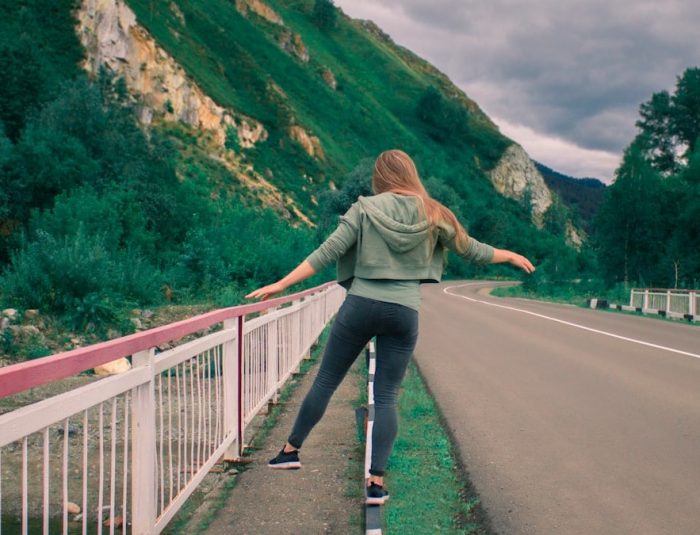 woman in gray jacket and blue denim jeans walking on gray concrete bridge during daytime